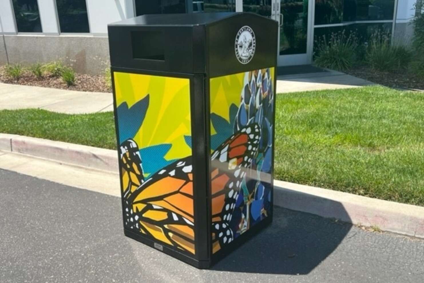 Black trash receptacle with butterfly print images on each side of the receptacle