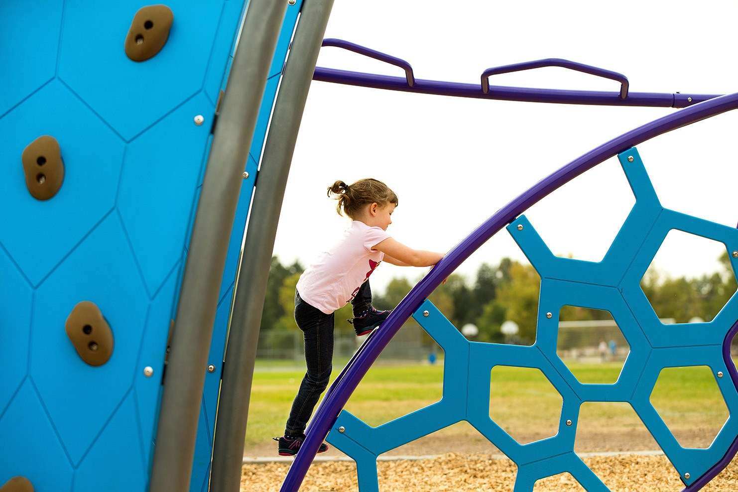 Image of a child in a pink shirt climbing across playground equipment