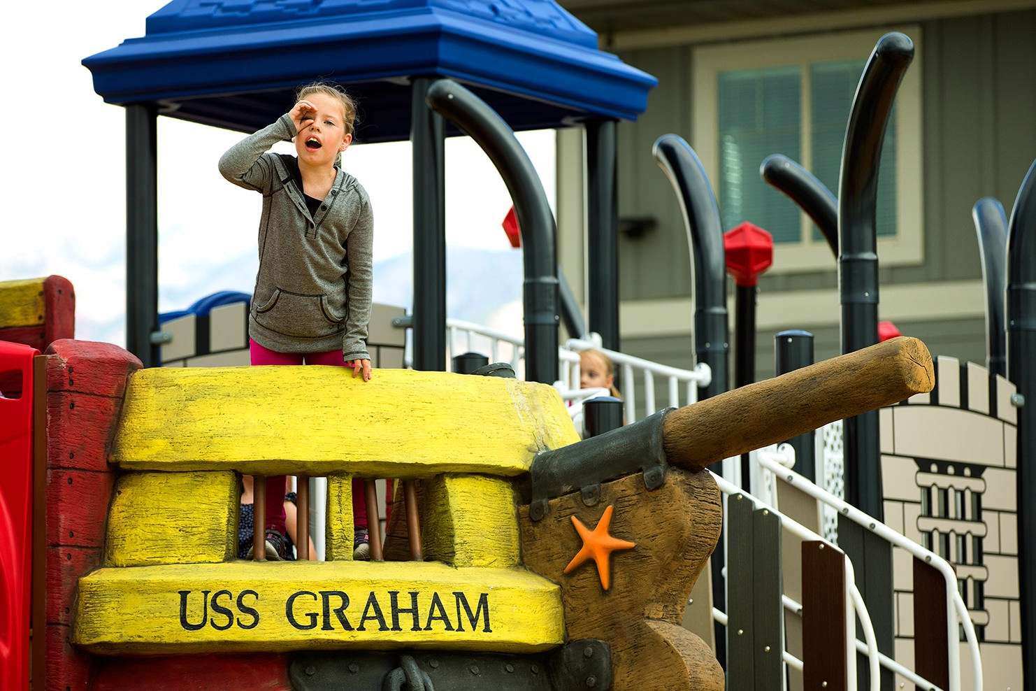 Image of a child making a telescope with her hand on top of the a playground ship called the USS Graham