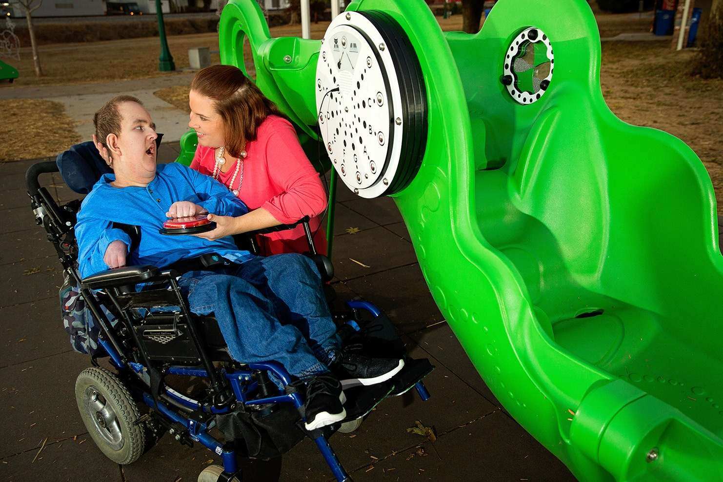 Image of a child in a wheelchair talking to a woman beside a green slide