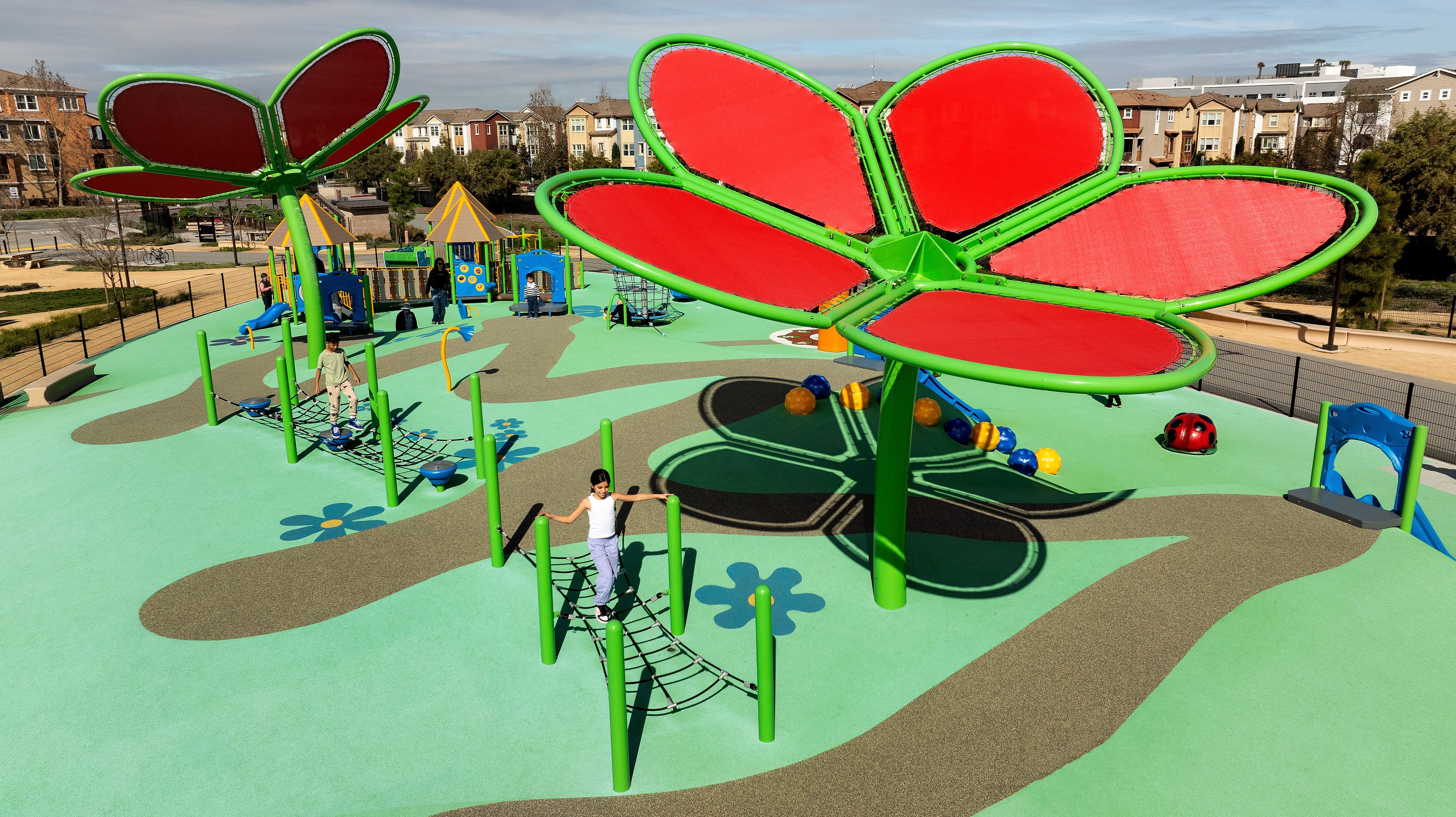 Image of a green playground with shade features resembling flowers and children walking across net bridges 