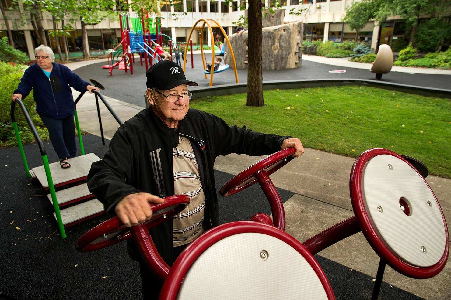 Image of an elderly man and elderly woman exercising on outdoor exercise equipment