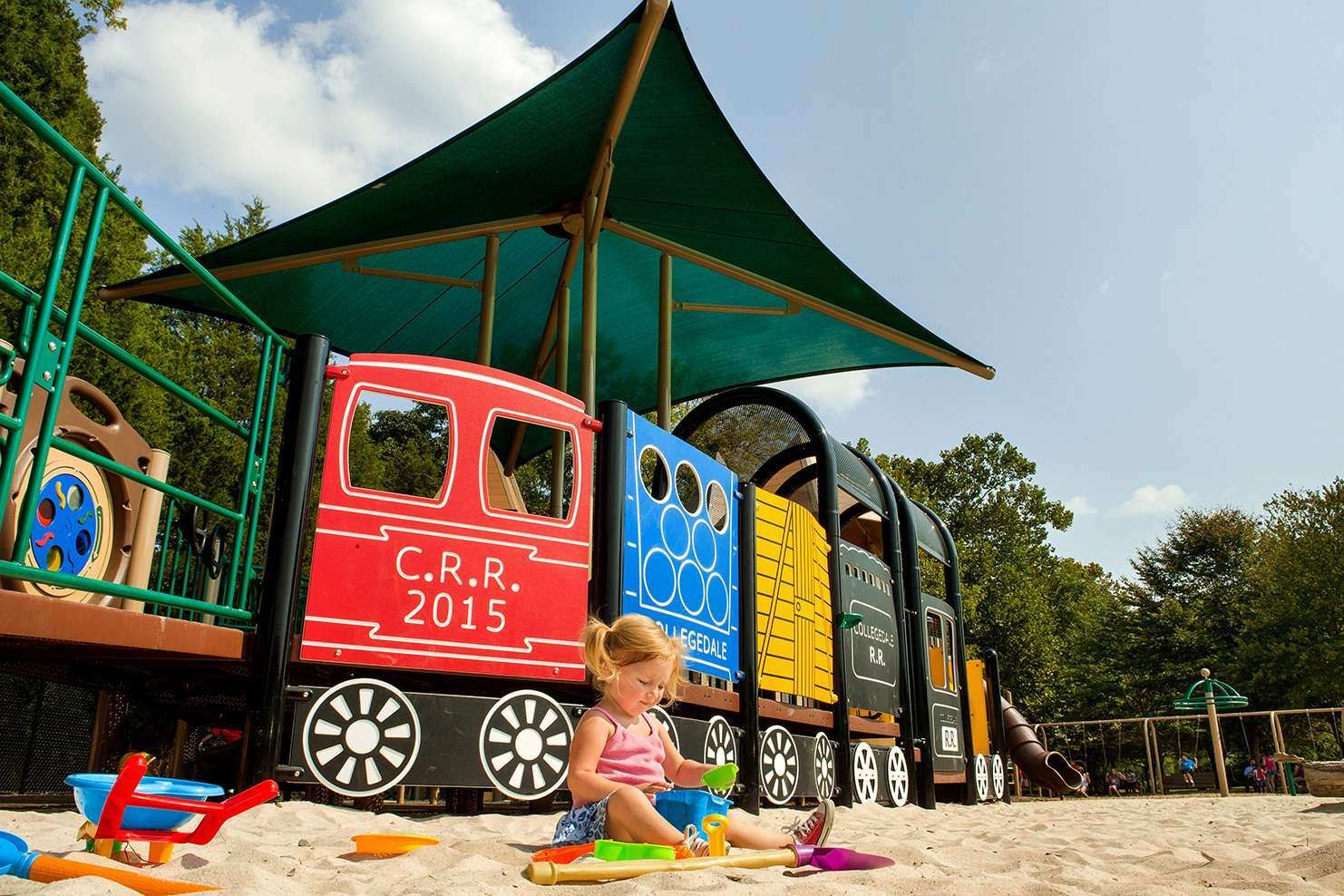 Image of a child playing in the sand in front of a train themed playground