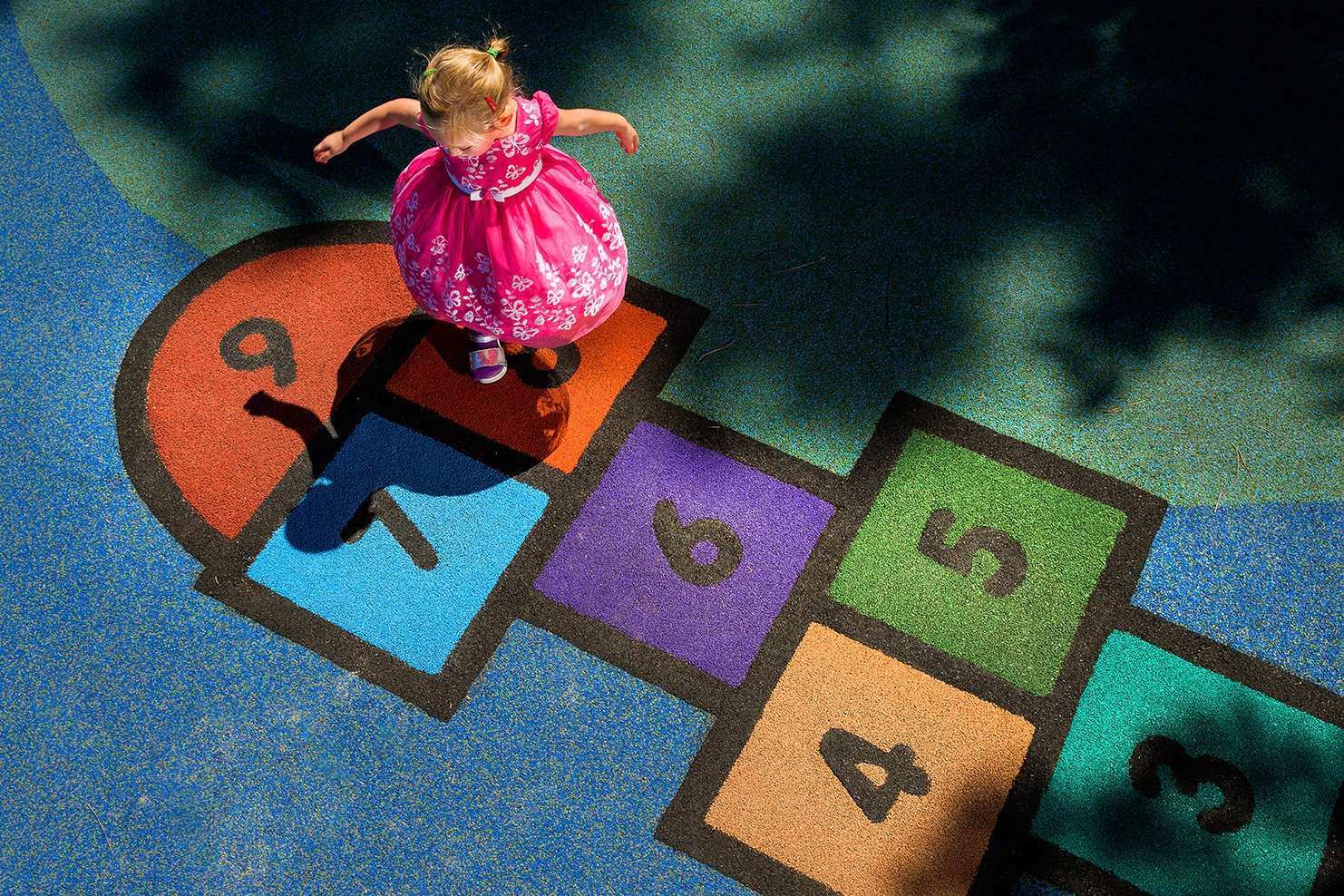 Image of a child in a pink dress playing hopscotch