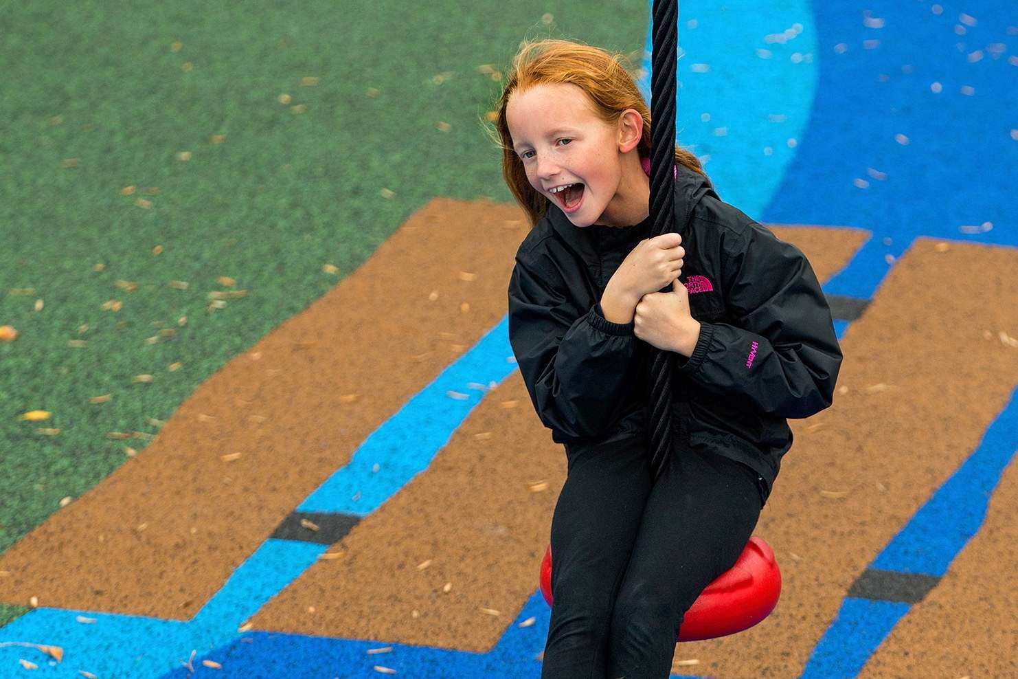 Image of a child in an all-black outfit riding on the seat of a playground zipline