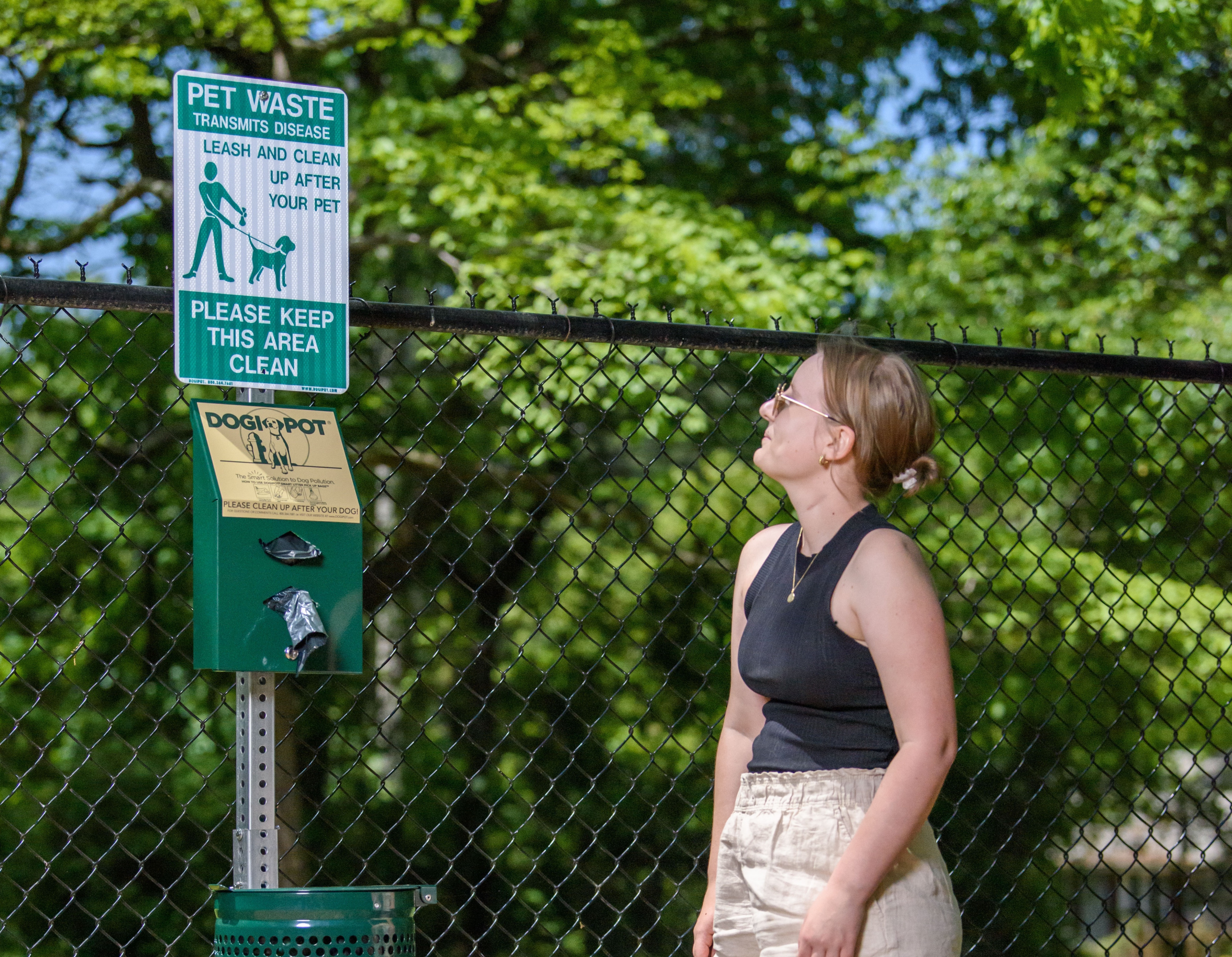 White Woman with black shirt and tan shorts standing in front of dog trashcan with a dog