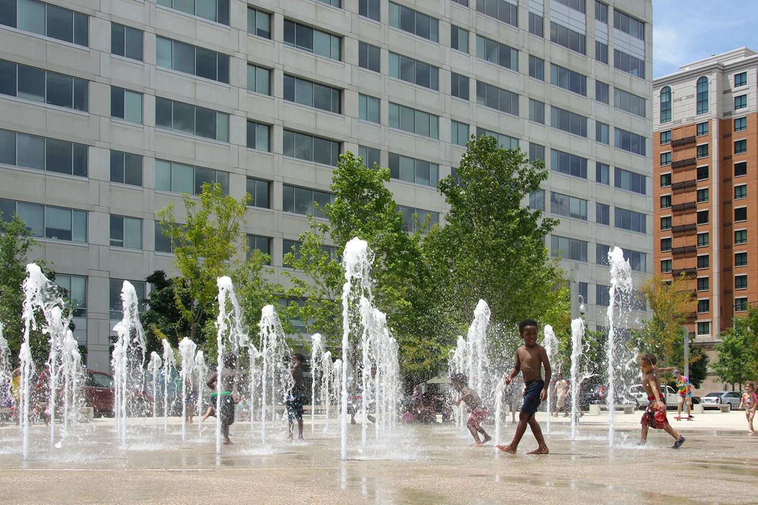 A group of children playing in an interactive splash pad with geyser style fountains in it