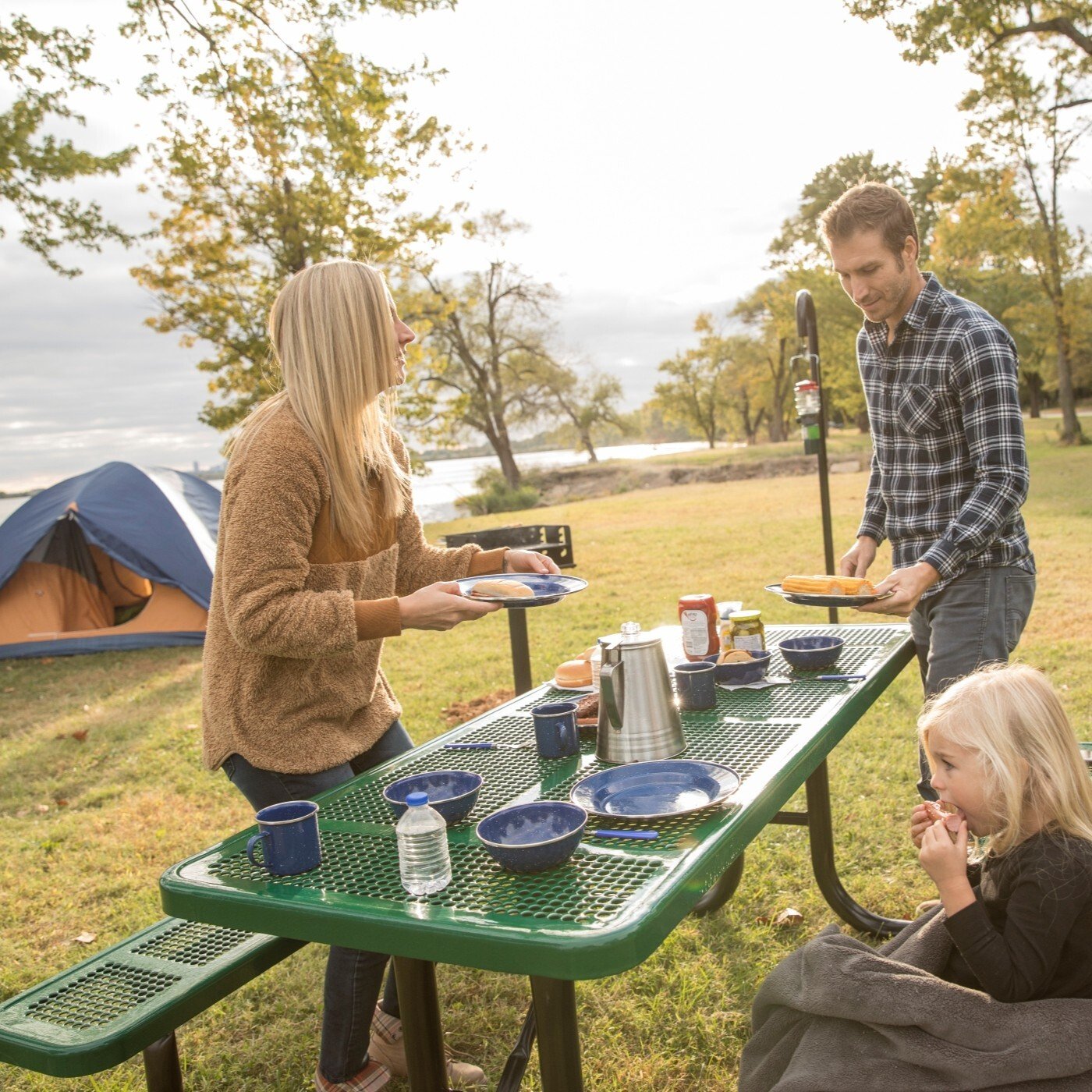 Image of a young woman, man, and child preparing to eat together at a green picnic table