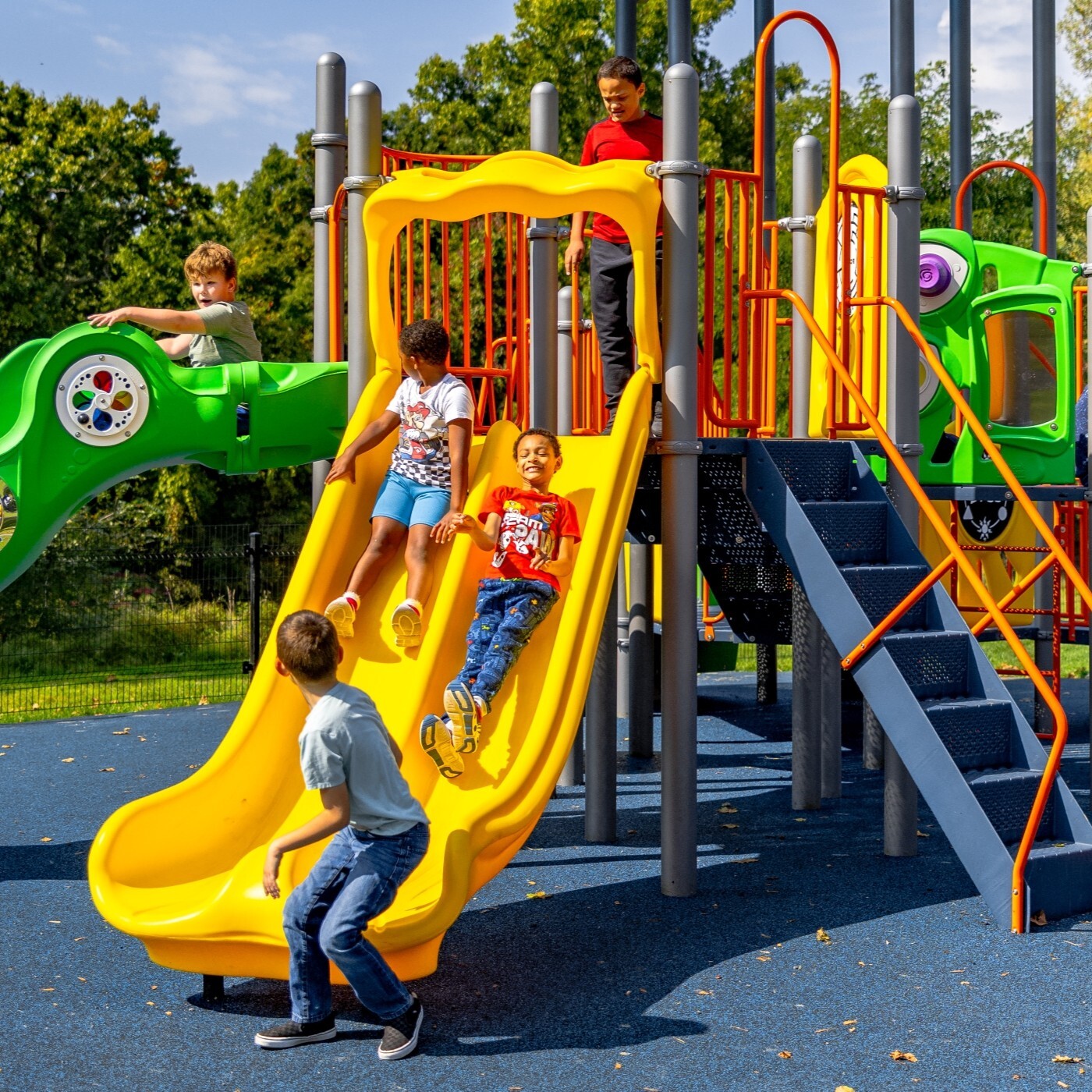 Image of a group of children going down a yellow slide, while a child waits to go down the slide
