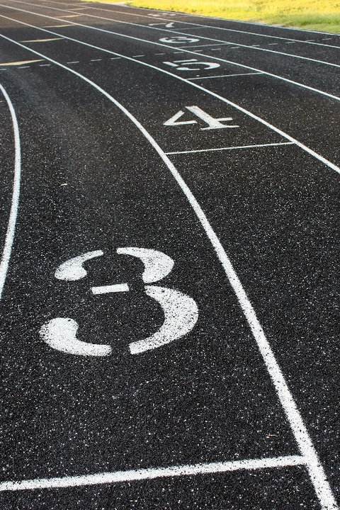 Image of a black surfacing for an outdoor track with white numbers for row lanes