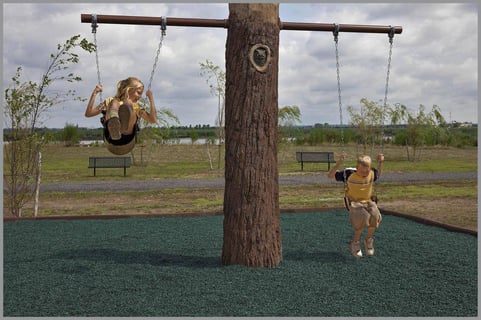 two children swinging on a swing set over an area filled with loose-fill rubber 