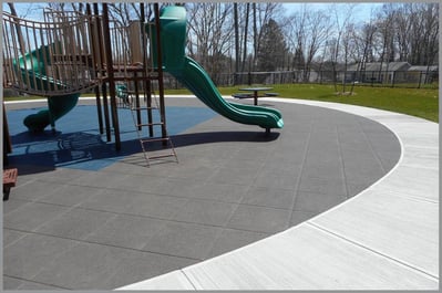 An image of a playground surrounded grey rubber tiling for safe play