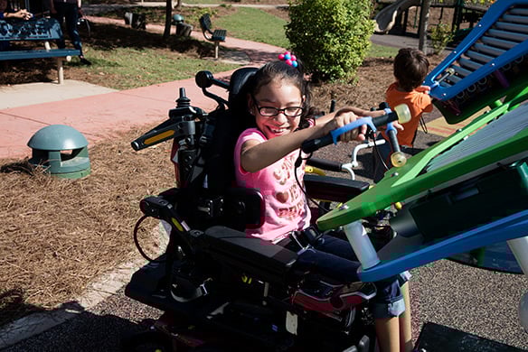 A young girl in a wheelchair playing with green playground equipment