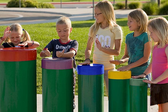 A group of children playing on green outdoor drums that gradually decrease in height 