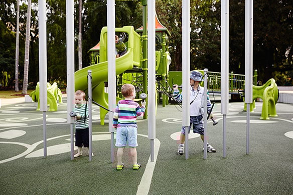 Three children playing together on outdoor musical instruments.