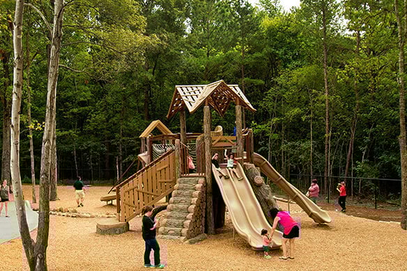 A playground resembling an all-wood playground set. There are also groups of people playing on the playground set as well