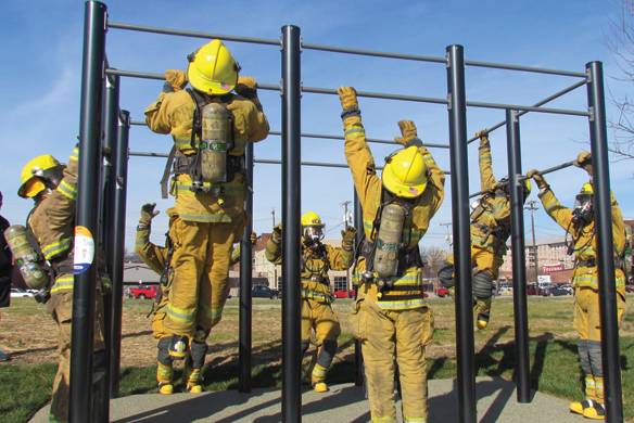 A group of fire fighters all in uniform performing pull ups on an outdoor pull up bar