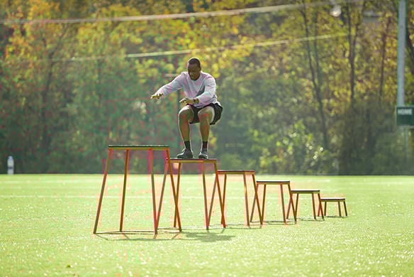 A man in a long sleeve grey shirt performing box jumps that gradually increase in height