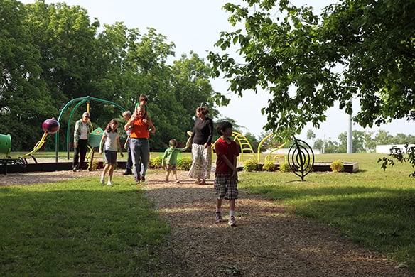 A group of children and adults walking down a shaded trail from a playground set