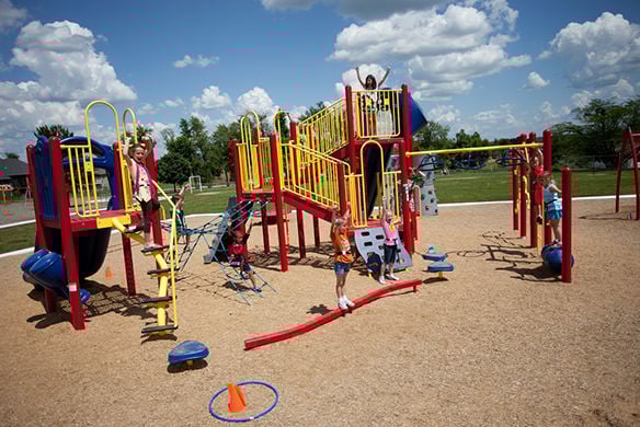 A group of children playing on a playground together. The children can be seen playing on different parts of the playground as well