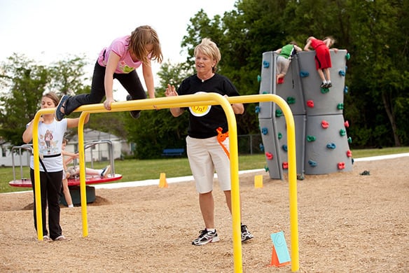 A young girl in a pink shirt crawling across yellow horizontal bars 