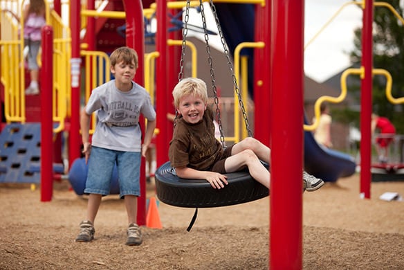 Two children swinging on separate tire swings on a playground