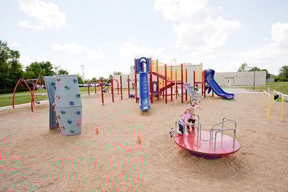 Two children playing on a red roundabout together in the front of a playground