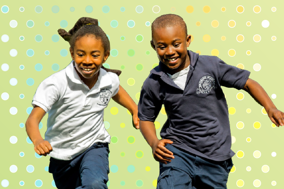 A young girl and boy both smiling as they run beside on another.