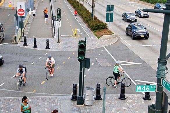 A crosswalk with people riding bikes across it as the cars sit idle in the road