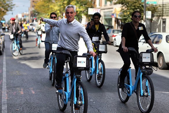 A group of people riding bikes on a road as one person in a grey sweater point towards the direction they were coming from