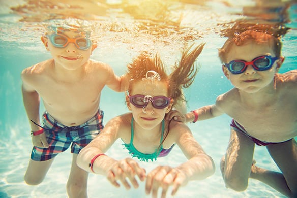 three children with googles on underwater staring into a camera before their picture was taken