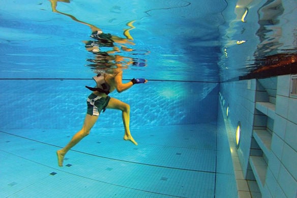The bottom half of someone walking towards the end of pool underwater