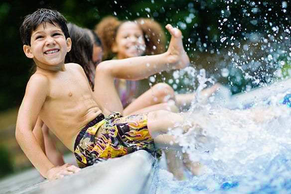 A group of kids playing in a pool by kicking the water with their feet