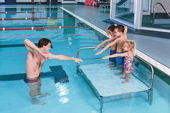 A group of children copying the pose of their teacher in a pool.