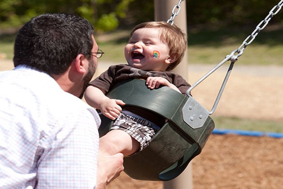 A baby smiling at its parent as the parent pushes the child in a green children's swing
