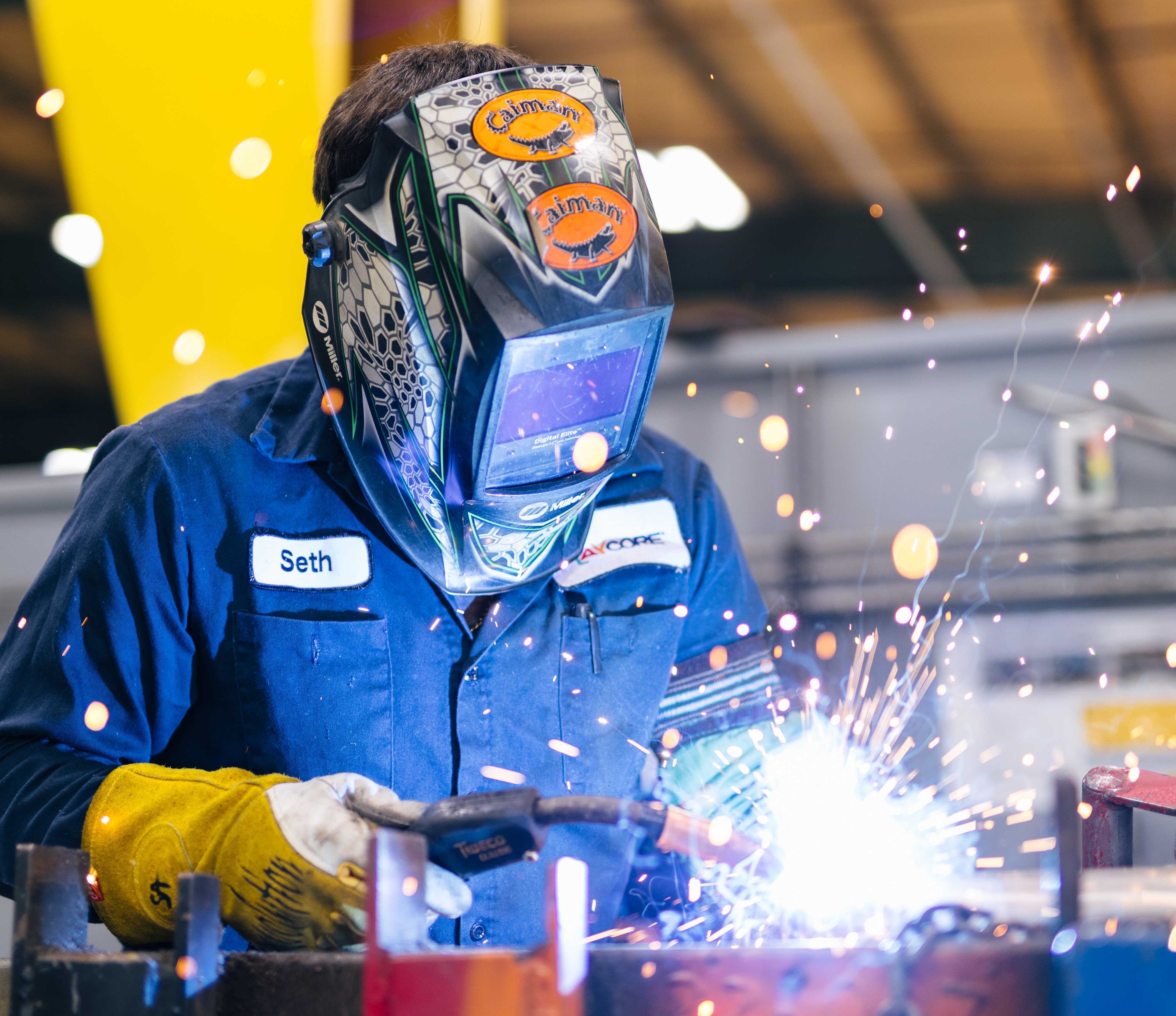 Welder welding a large piece of steel wearing welder helmet with yellow protective gloves