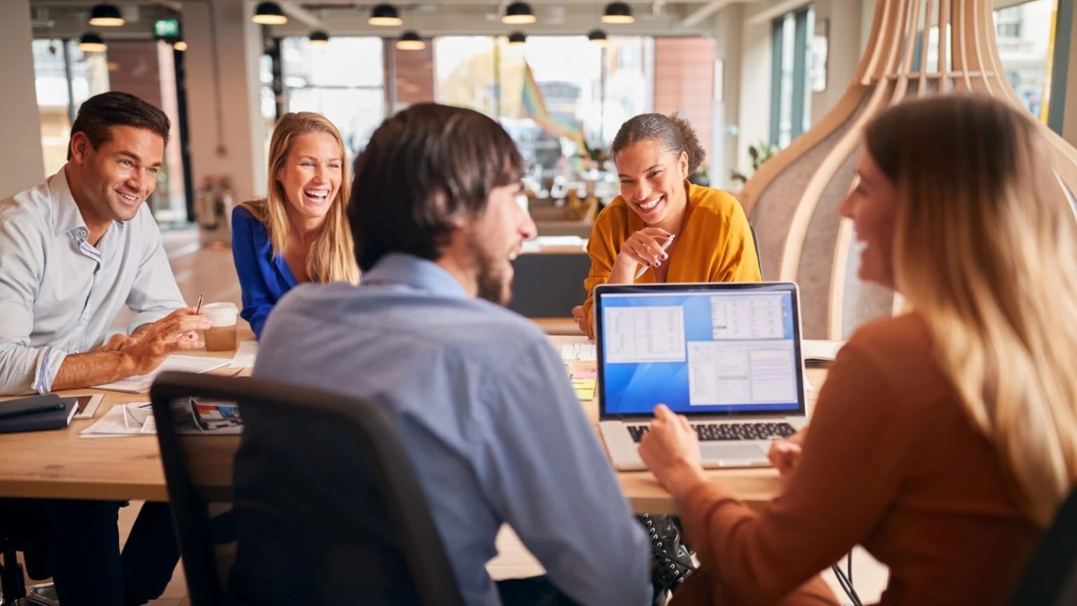 Group of 5 people sitting at a table smiling and looking at a laptop computer