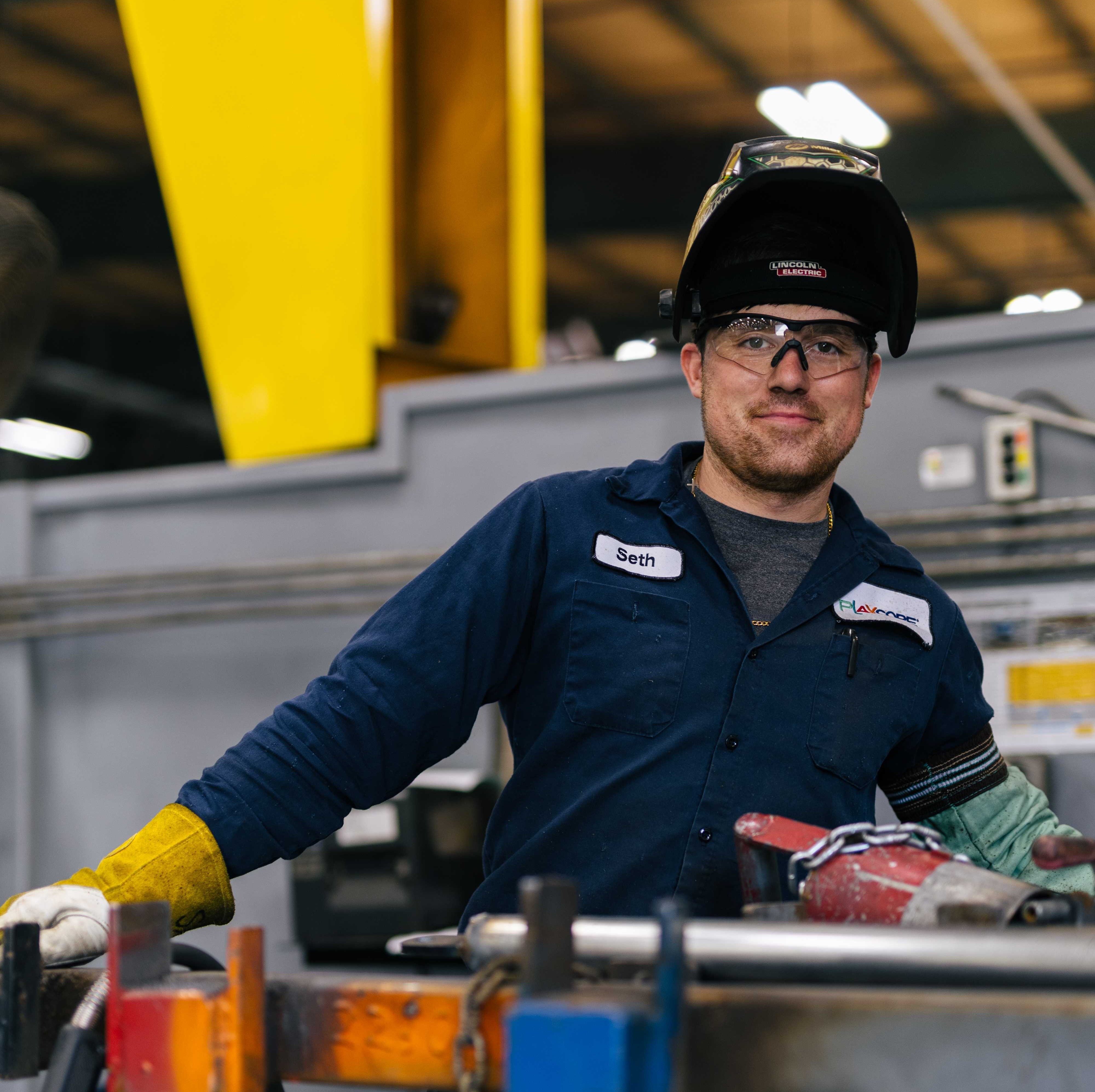 White man with a welders uniform with blue jumpsuit and protective eyewear