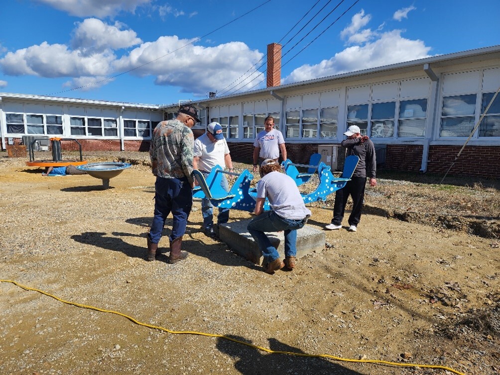 5 men installing a piece of blue playground equipment