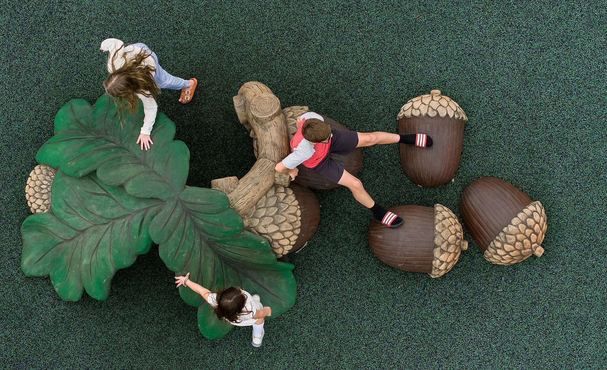 Image of three children playing on a sculpture of acorns and leaves