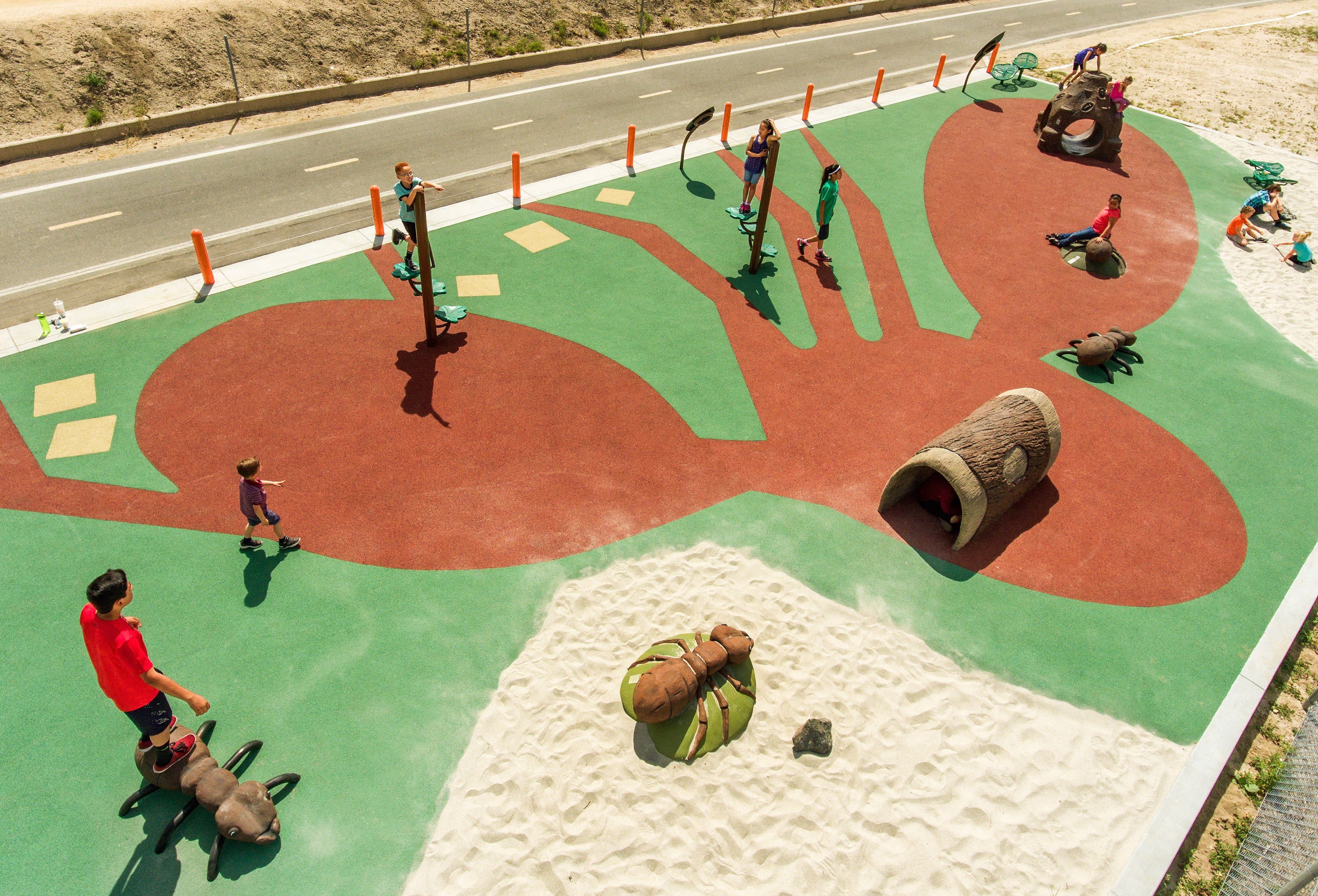 Image of people walking on a playground. The playground rubber surface depicts an ant.