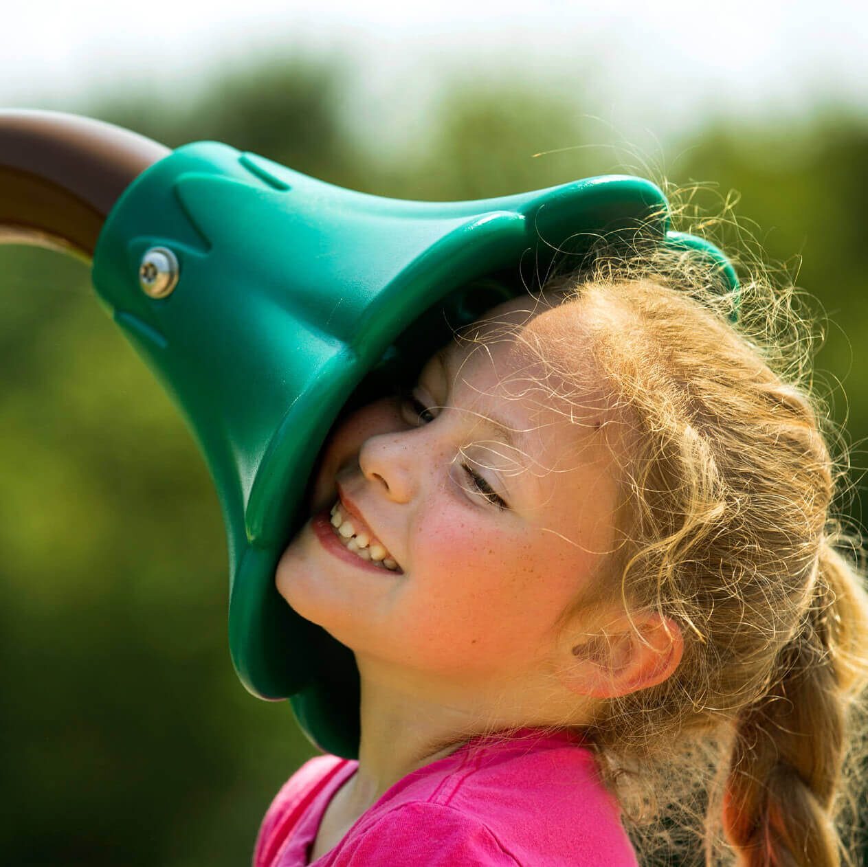 Young girl smiling while using a sensory play element on an inclusive playground, encouraging auditory engagement and sensory development.
