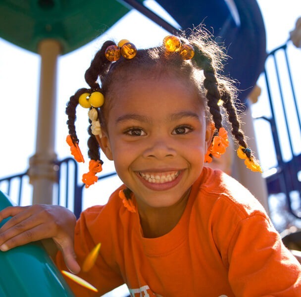 Smiling young girl playing on an inclusive playground, promoting social-emotional development and outdoor play for whole child growth.