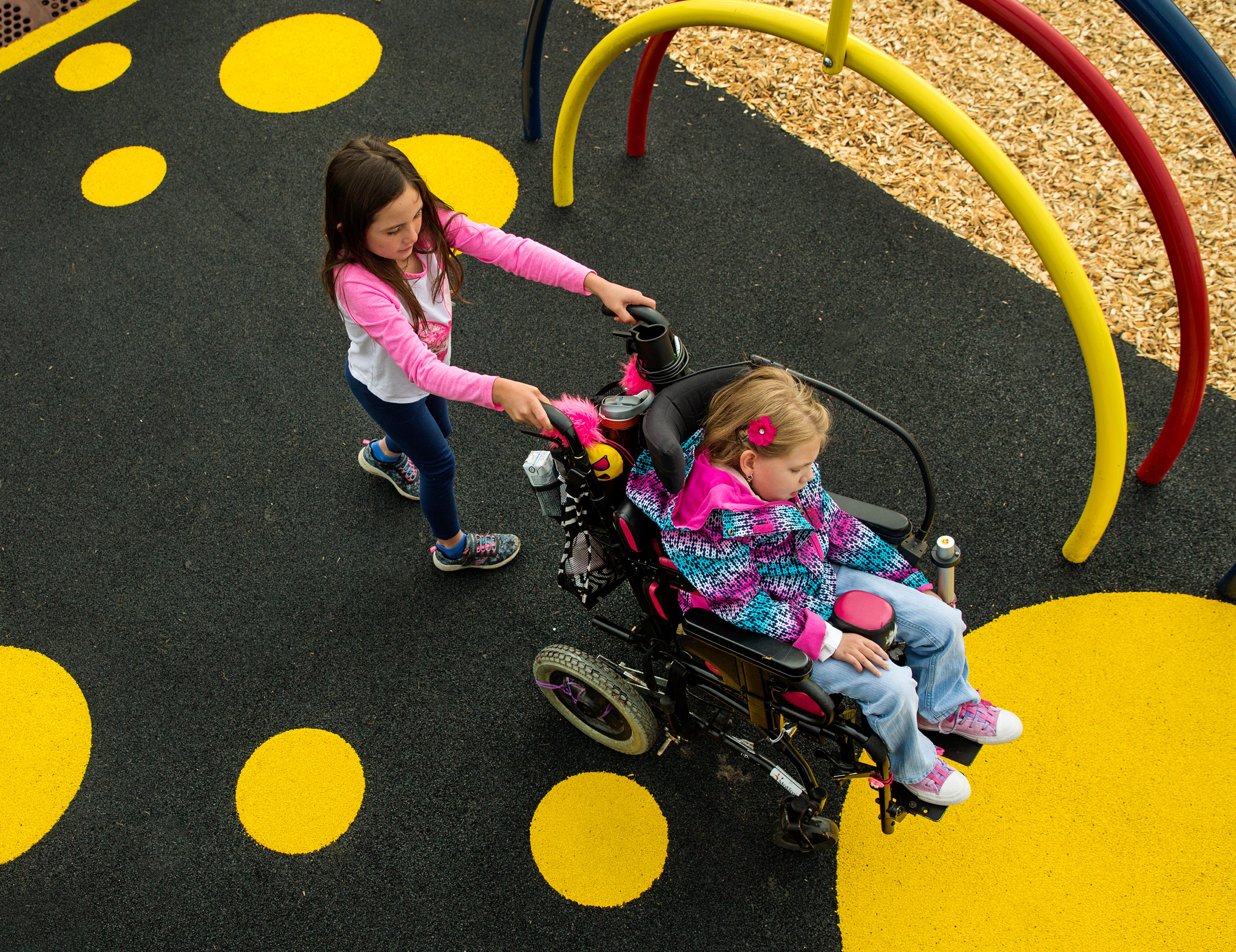 Child pushing another child in mobility device across Unitary Saftey Surfacing