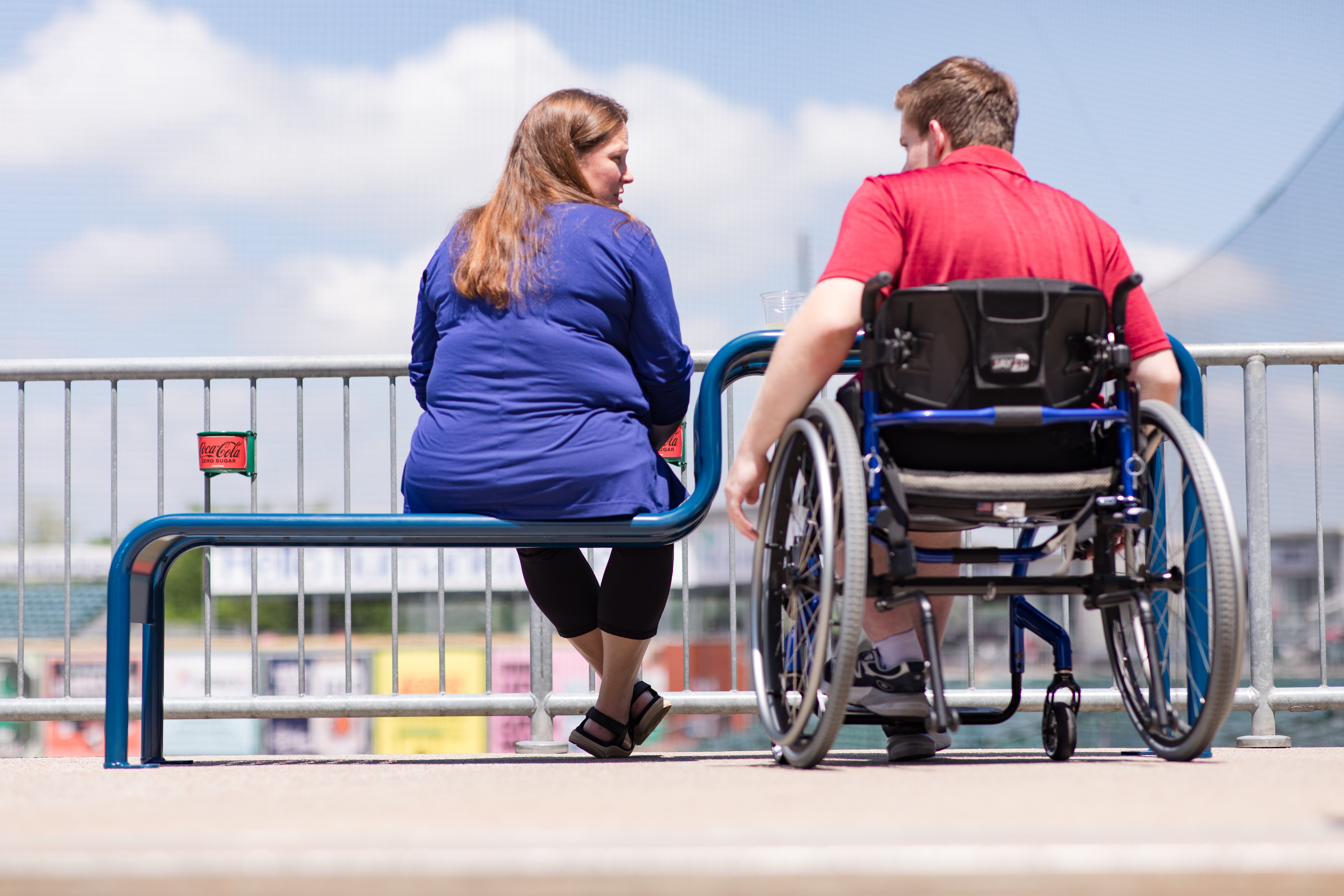 Man in mobility device with woman using inclusive bench