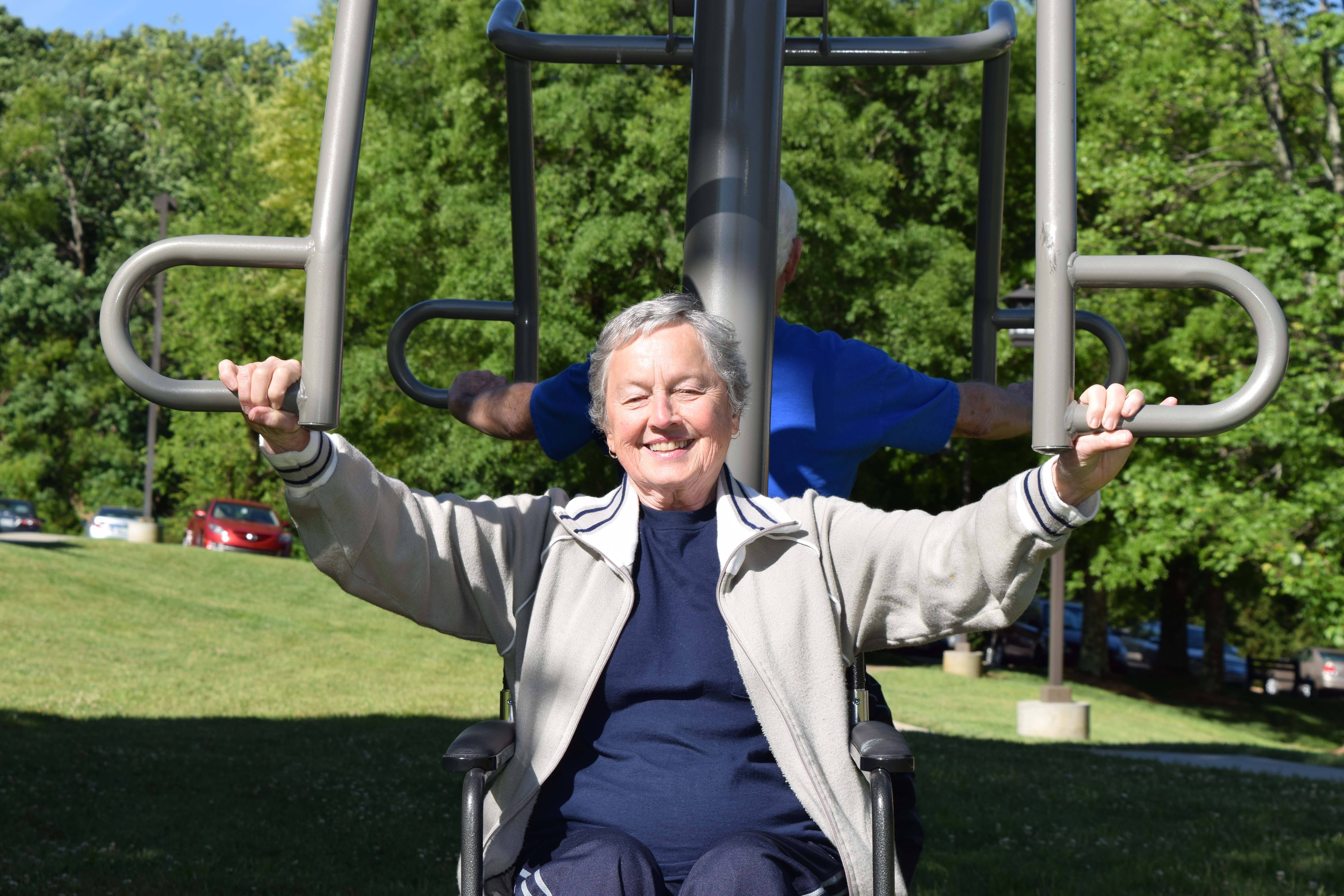 A senior woman in a mobility device using outdoor fitness equipment