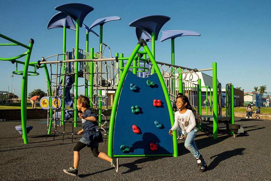 Children chasing one another around a green and blue playground