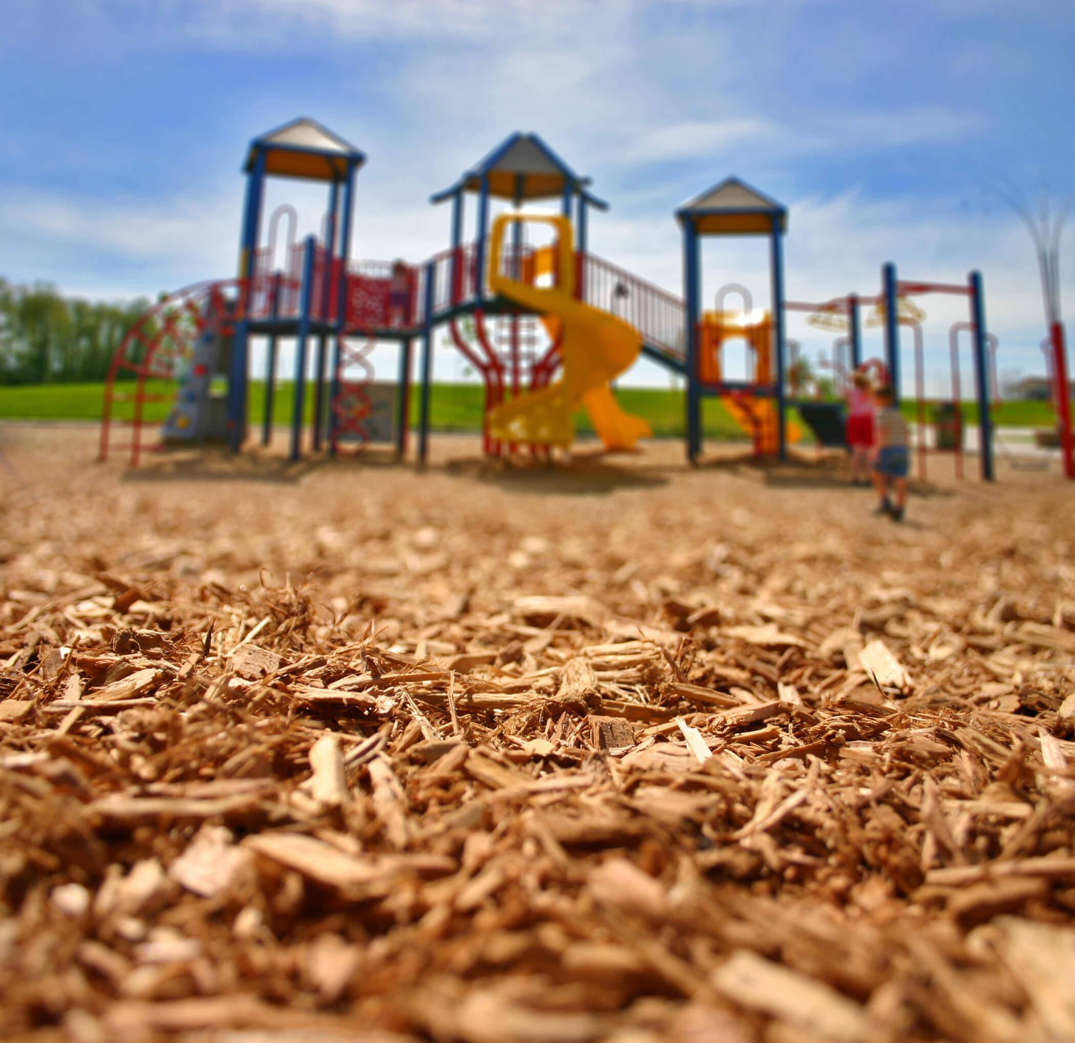 A close-up of loose-fill playground surfacing with a playground out of focus in the background