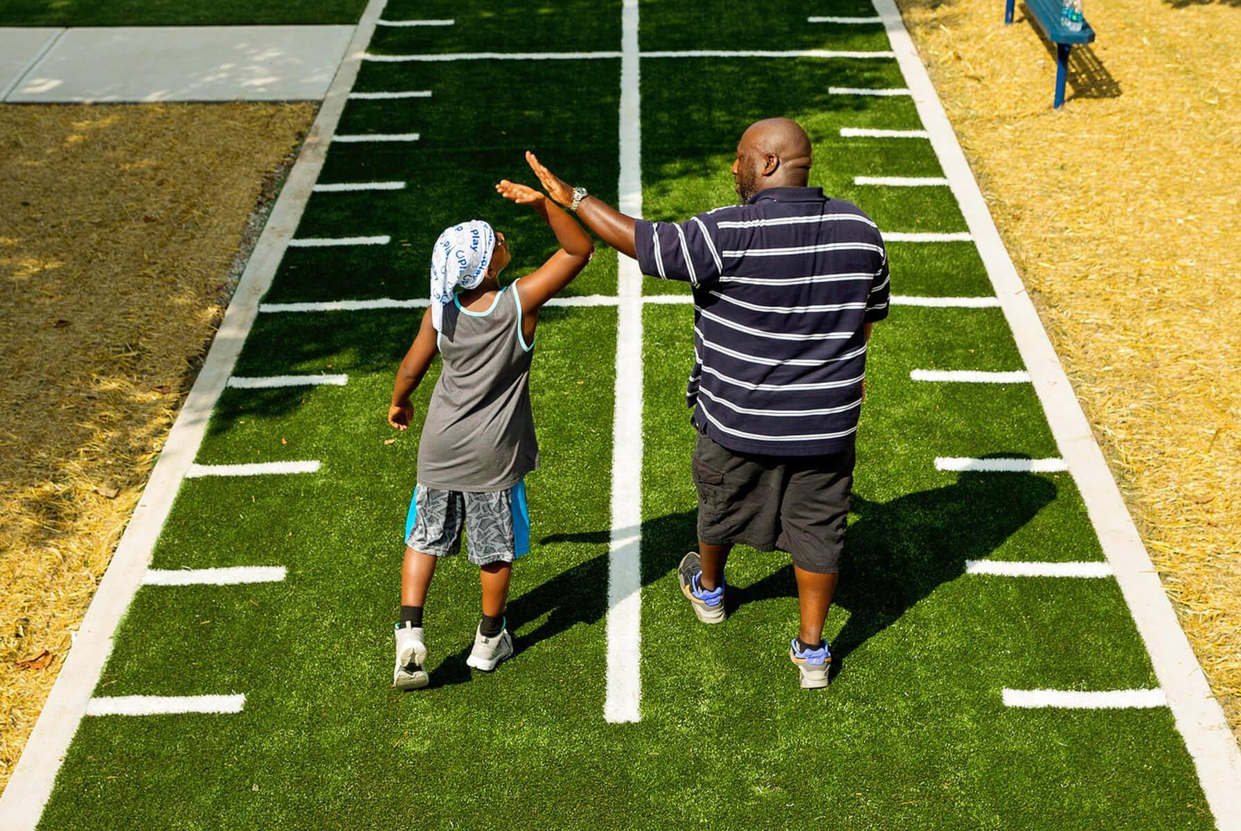 Child and adult high-five on playground football field.