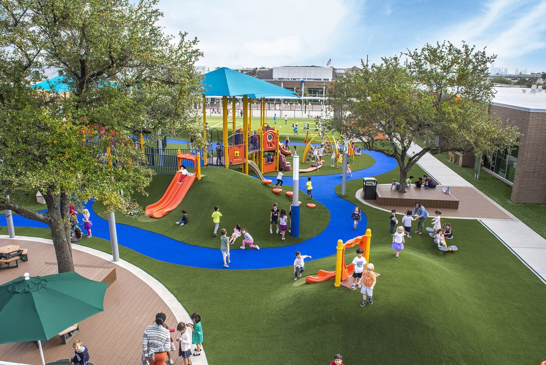 Children playing on colorful playground with slides, turf hills, and shaded structures.